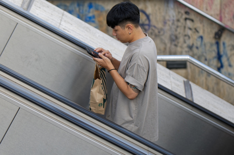 20 - Person standing on an escalator holding a Starbucks paper bag while using a phone